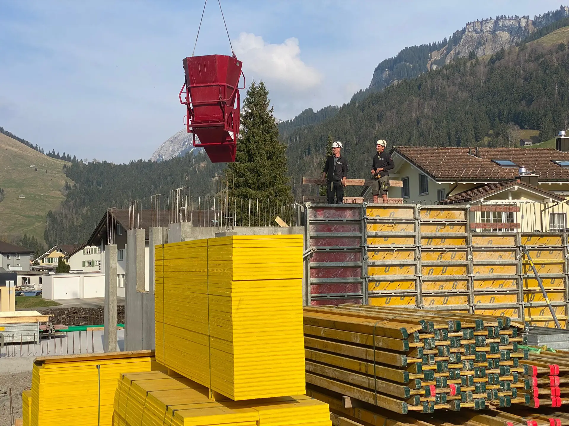 Baustelle in Unteriberg: Kran hebt einen roten Betonkübel über gelbe Schalungsplatten, Arbeiter auf der Schalung
